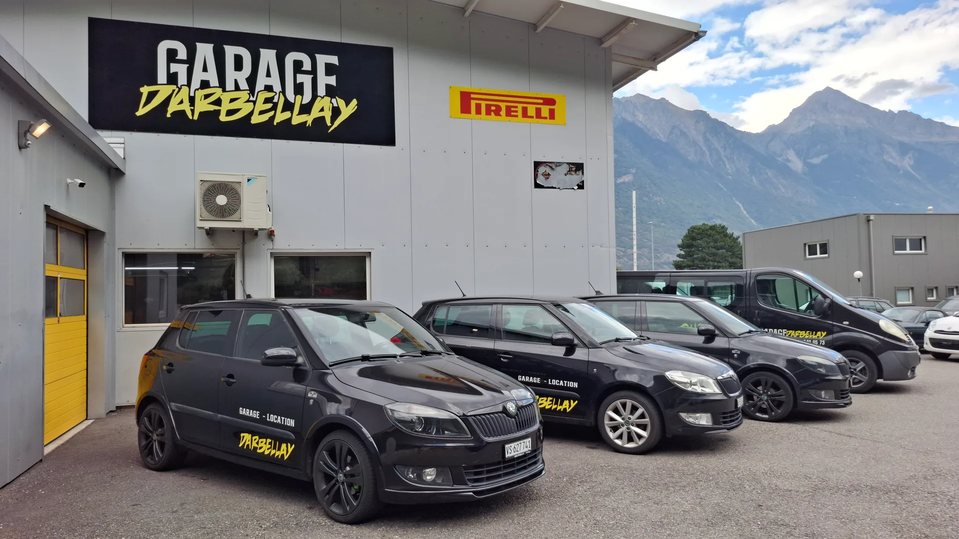 Trois voitures de location noires du garage Darbellay devant les portes jaunes de l'atelier